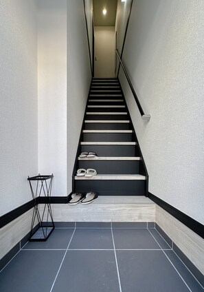 Eine moderne Treppe mit Metallgeländer, Schuhablage und einem Paar Hausschuhen auf den Stufen.