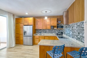 A modern kitchen with wooden cabinets, a stainless steel refrigerator, a stone backsplash, and a granite countertop. - Luxury Gateway 2BR Bayahibe Pool Beach (Bayahíbe La Romana)