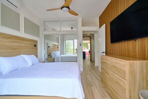 A bedroom with a large bed, a ceiling fan, a TV mounted on the wall, and a wooden wardrobe. - Luxury Gateway 2BR Bayahibe Pool Beach (Bayahíbe La Romana)