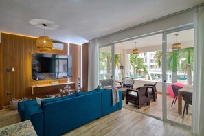 A modern living room with a large blue sofa, a flat-screen TV, and a balcony with outdoor seating. - Luxury Gateway 2BR Bayahibe Pool Beach (Bayahíbe La Romana)