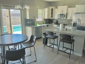 A modern kitchen with white cabinets, a stainless steel refrigerator, and a dining area with a round table and bar stools. - Enjoyable 3-bedroom Pool house in vibrant El Paso steps away from sports complex (El Paso)