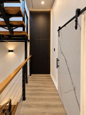 Un interior moderno con una escalera de madera, una puerta corredera oscura y una pared de mármol.