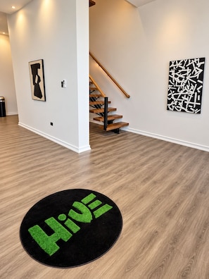 Un interior moderno con una escalera de madera, un felpudo negro y verde, y arte abstracto en las paredes.