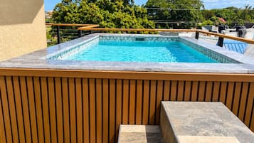 A swimming pool with a wooden deck and steps leading to it, surrounded by greenery.