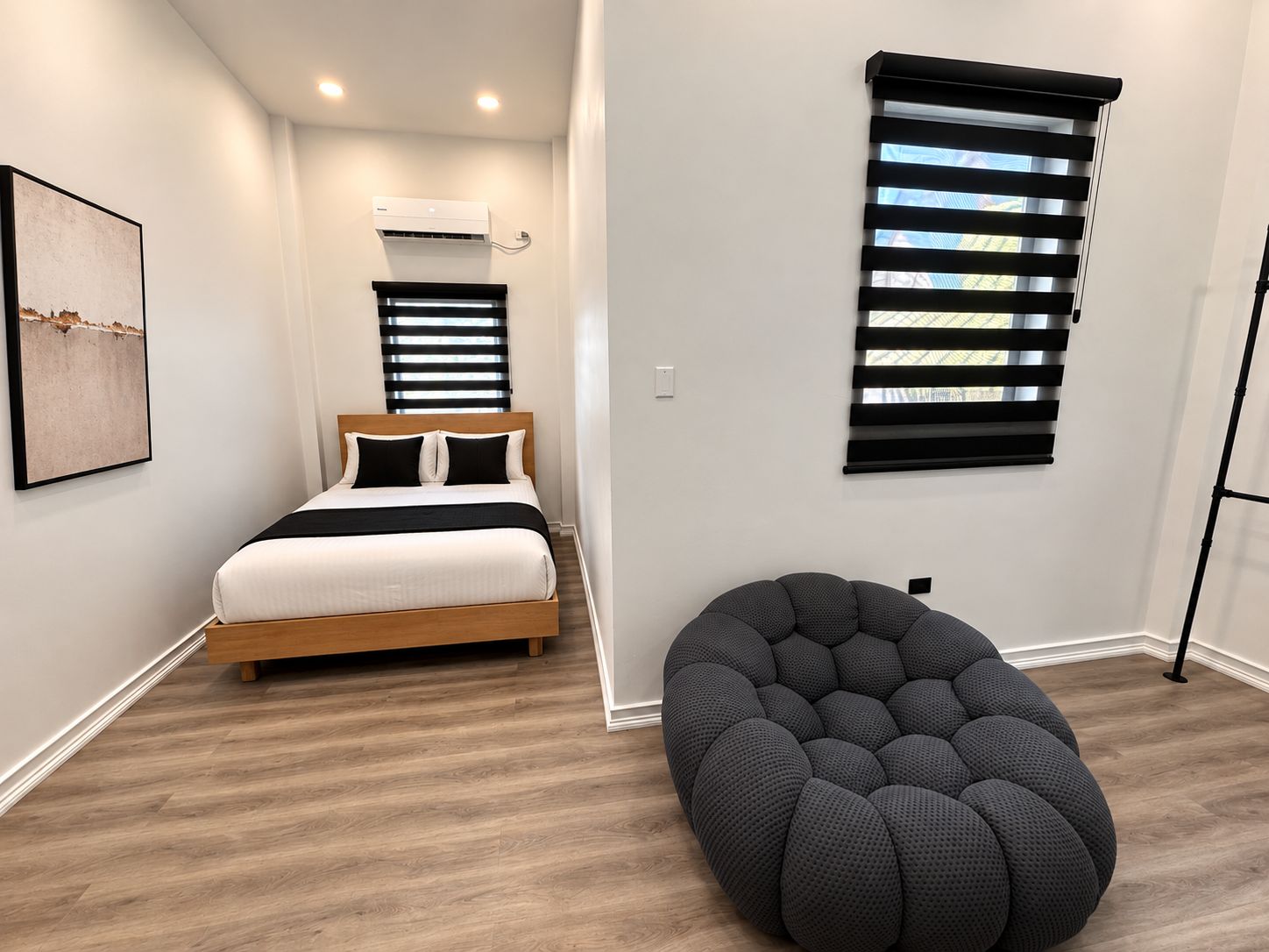 A bedroom with a bed, a wall-mounted air conditioner, and a window with blinds.