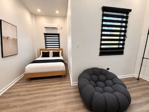 Een slaapkamer met een bed, een wandairconditioner en een raam met zonwering.