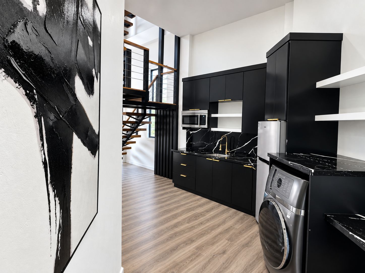 Une cuisine moderne avec des meubles de couleur noire, un lave-linge en acier inoxydable et un escalier en bois.