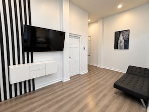 Un salon moderne avec un téléviseur à écran plat fixé au mur, un canapé noir et un plancher en bois.