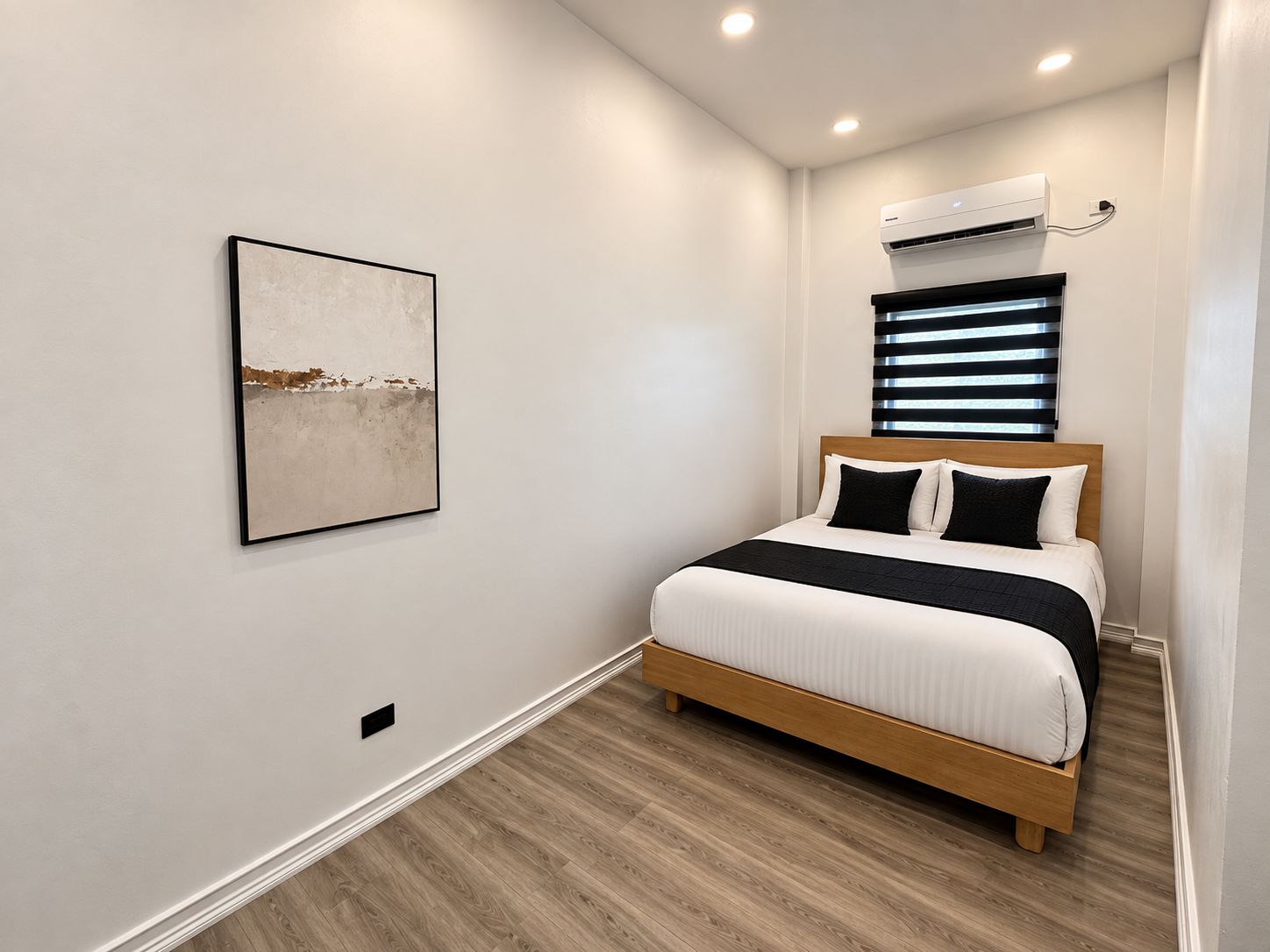 A bedroom with a bed, a wall-mounted air conditioner, and a framed picture.