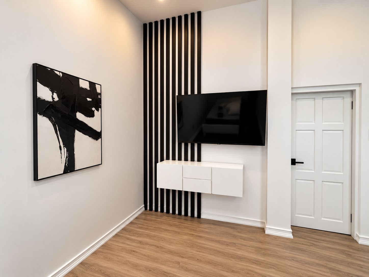 A hallway with a black and white striped wall, a mounted TV, a white console unit, and a door.