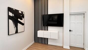 A hallway with a black and white striped wall, a mounted TV, a white console unit, and a door.