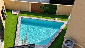 A rectangular pool with a clear blue water surface, surrounded by artificial grass, and a wooden fence with a green logo.
