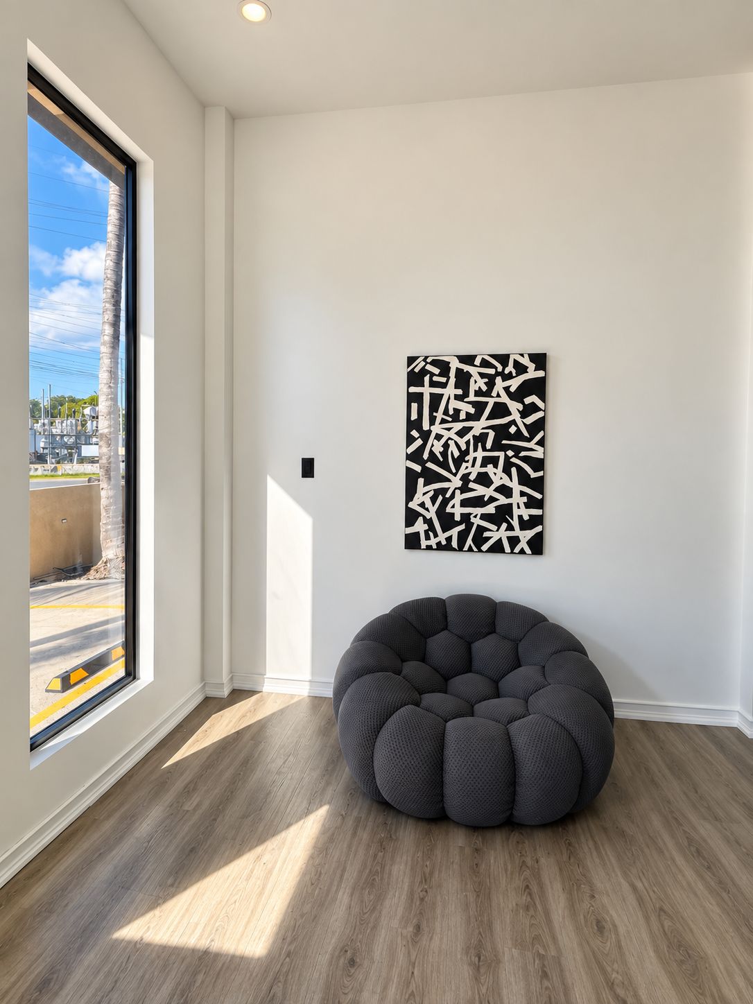 A room with a large window, a round bean bag chair, and a wall-mounted abstract art piece.