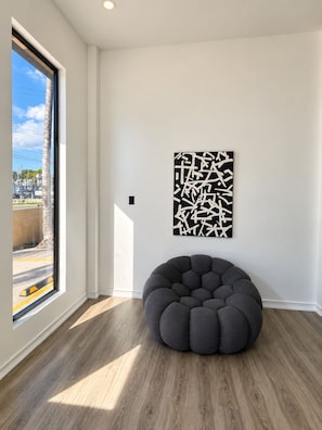 Een kamer met een groot raam, een ronde loungestoel en een wanddecoratie met abstracte kunst.