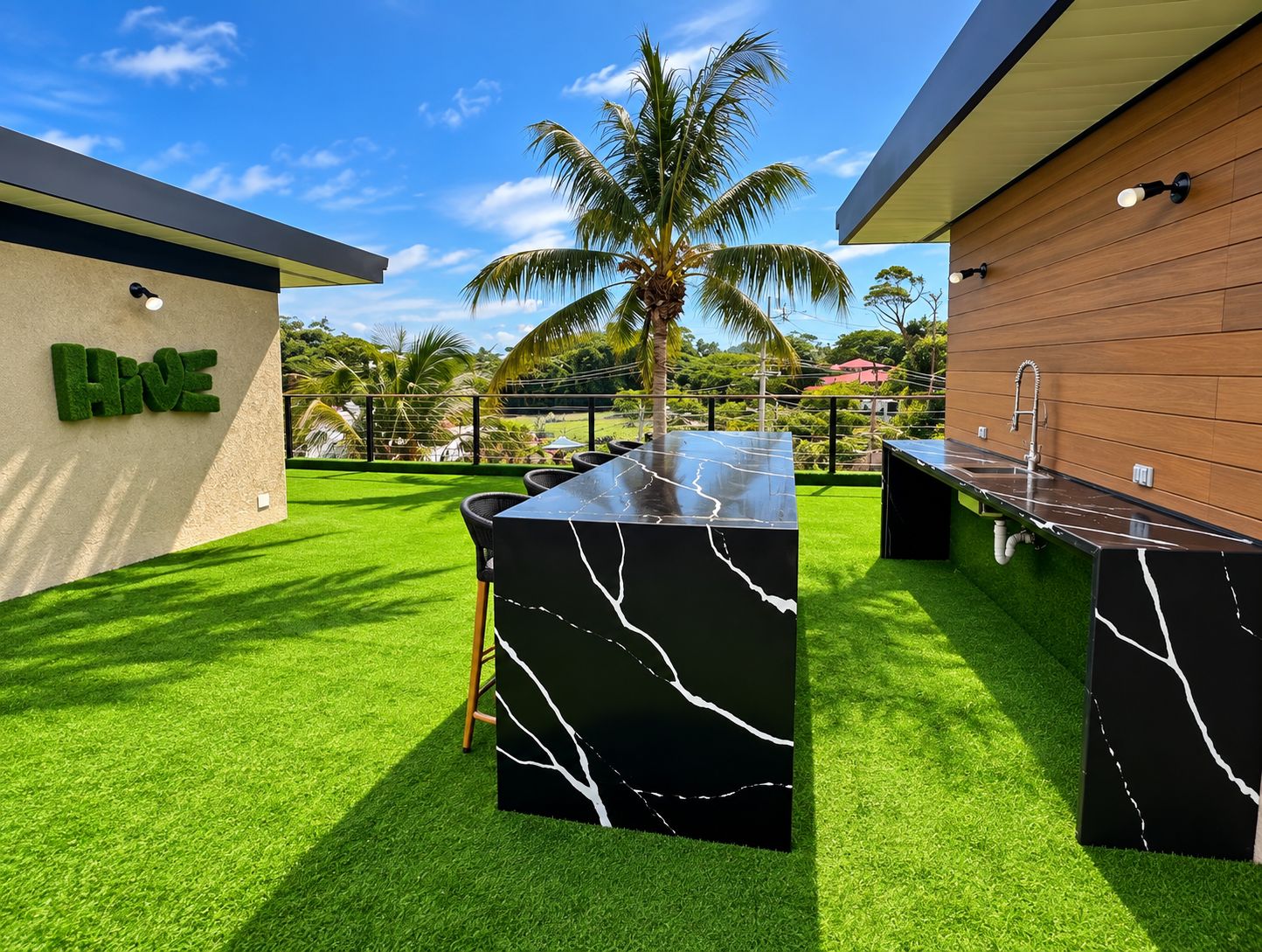 An outdoor bar area with a marble countertop, artificial grass, and a sign that reads 'Hive'.