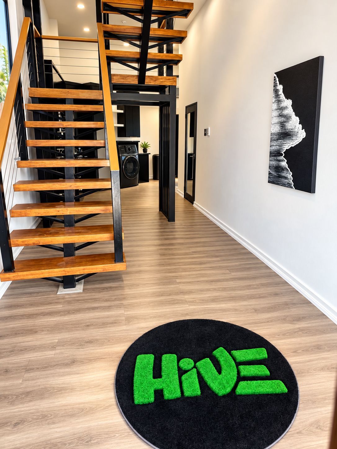 A modern interior with a wooden staircase, a black rug with green text, and a framed picture on the wall.