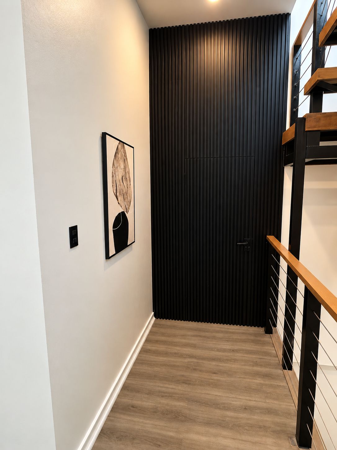 A hallway with a wooden floor, a black door, and a staircase with wooden railings.