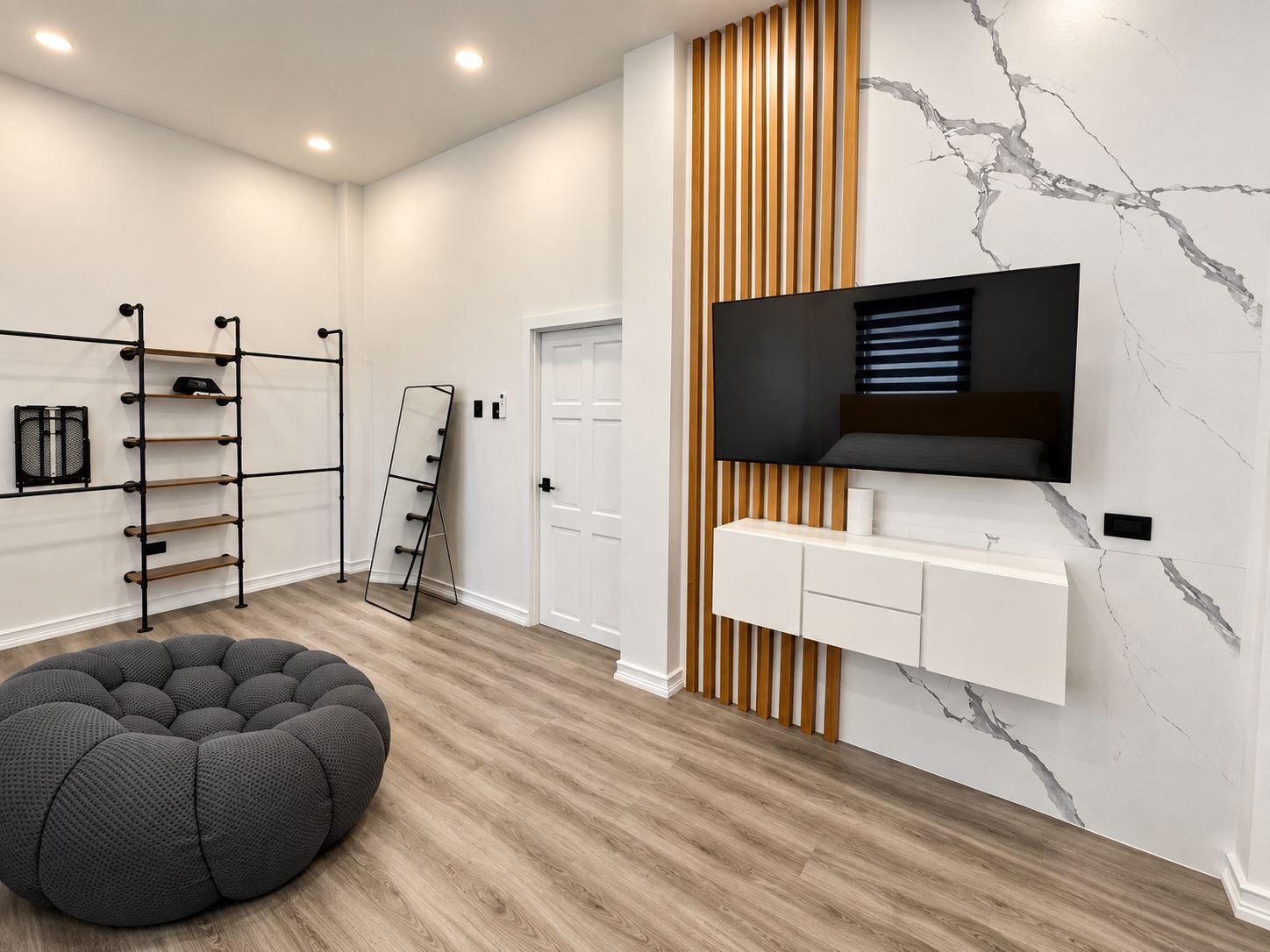 Ein modernes Wohnzimmer mit Holzboden, einem schwarzen Sitzsack, einem an der Wand montierten Fernseher und einem weißen Schrank darunter.