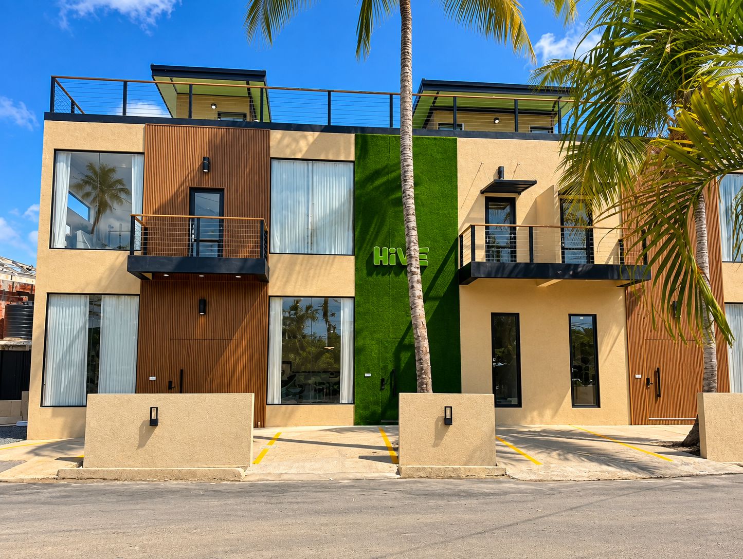 Un edificio moderno a due piani con una fascia verde verticale, balconi e una palma in primo piano.