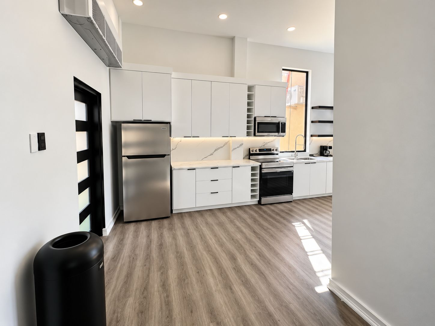 A modern kitchen with white cabinetry, stainless steel appliances, and a wooden floor.