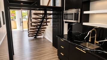 A modern kitchen with black cabinetry, a stainless steel microwave, and a black countertop.