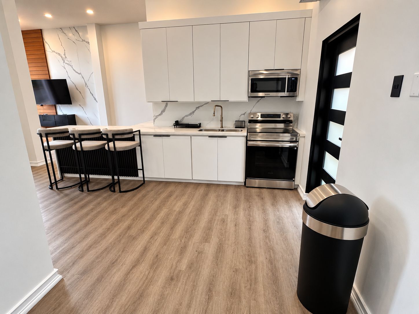 A modern kitchen with white cabinets, a stainless steel oven, a microwave, and a black trash bin.