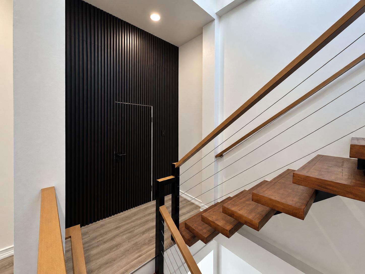 A modern staircase with wooden steps and metal railings, leading to a door with vertical black slats.