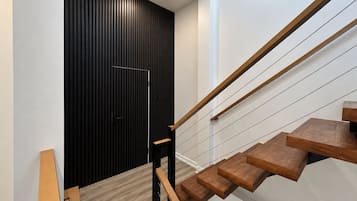 A modern staircase with wooden steps and metal railings, leading to a door with vertical black slats.