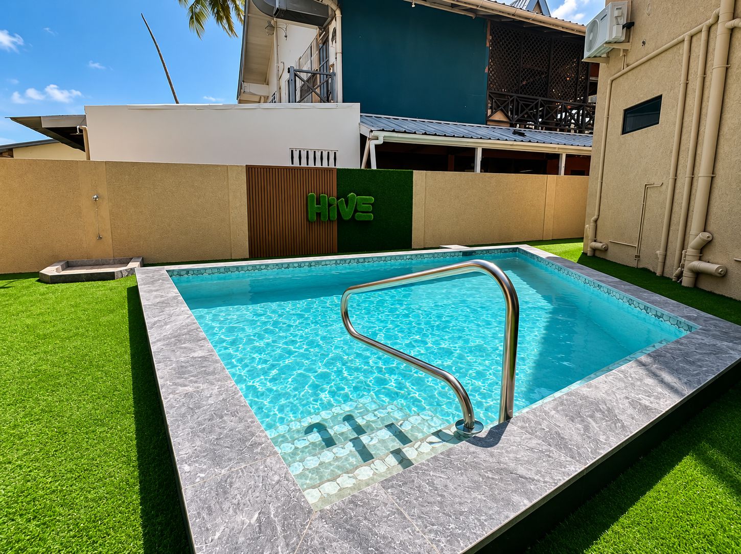 Una piscina con una escalera de metal, rodeada de césped artificial y un borde de baldosas.