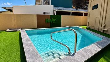 Una piscina con una escalera de metal, rodeada de césped artificial y un borde de baldosas.