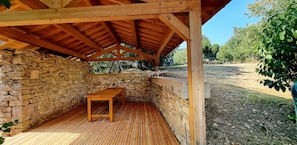 Ein überdachter Außenbereich mit einer Steinmauer, einer Holzbank und einem Holztisch.