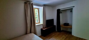 Ein Zimmer mit einem Bett, einem Vorhangfenster, einem Fernseher und einem Regal mit einem Topf.
