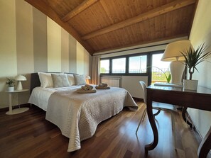 A bedroom with a wooden ceiling, a bed with a white bedspread, a desk with a lamp, and a view of the outdoors through a window. - Almond Vista, Lucca Roof Garden (Lucca)