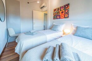 A hotel room with two beds, a chair, a painting, and an air conditioning unit. - Almond Vista, Lucca Roof Garden (Lucca)