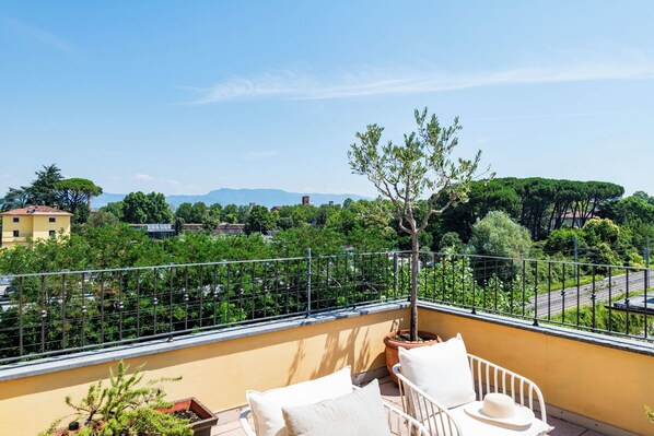 A balcony with a yellow wall, a metal railing, and a view of a green landscape with trees and buildings. - Almond Vista, Lucca Roof Garden (Lucca)