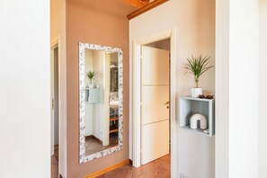 A hallway with a mirror, a plant, and a shelf with a vase and glasses. - Almond Vista, Lucca Roof Garden (Lucca)