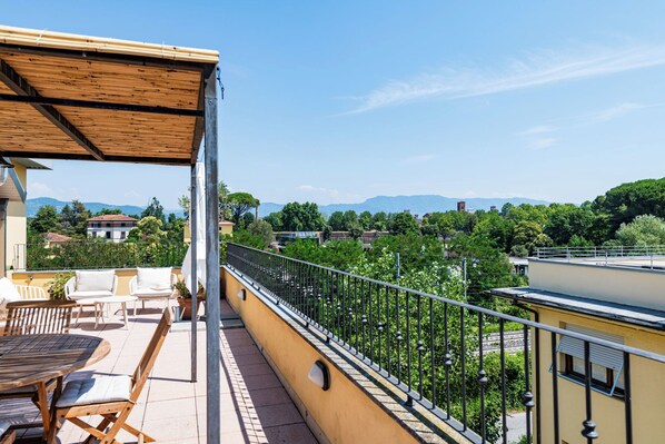 A balcony with outdoor furniture, a view of a residential area, and a mountain in the distance. - Almond Vista, Lucca Roof Garden (Lucca)