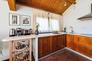 A kitchen with wooden cabinets, a white countertop, a coffee maker, a toaster, and a vase with flowers. - Almond Vista, Lucca Roof Garden (Lucca)