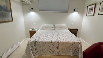 Et soveværelse med en seng, sengeborde, en rød stol, en loftslampe og et vindue med persienner.