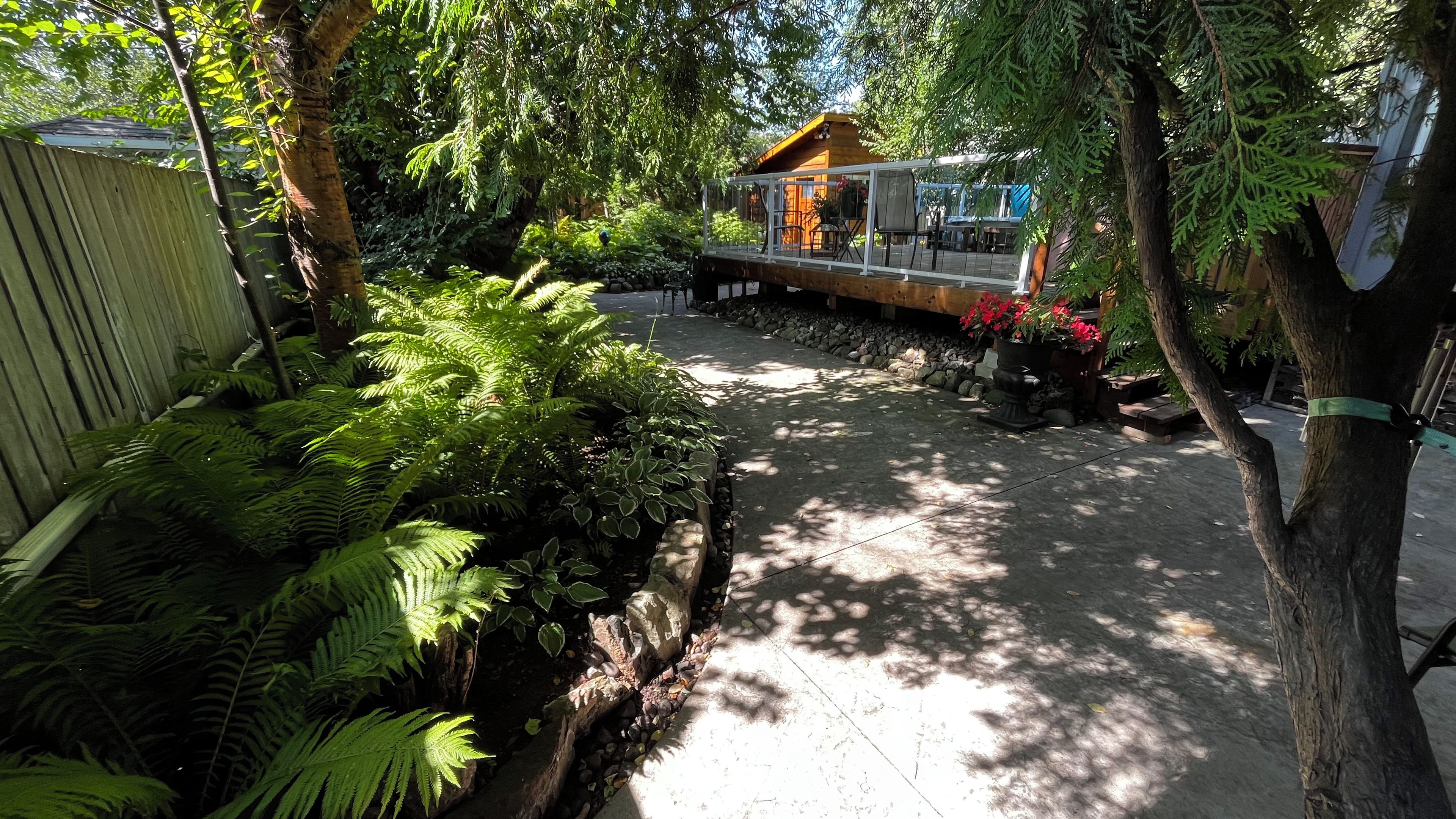 A garden area with a wooden deck, potted plants, and a building with a glass enclosure.