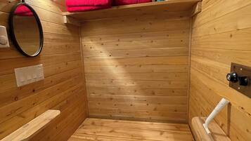 Un sauna de madera con bancos, una estantería con toallas, un espejo y un perchero.