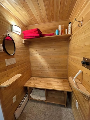Ein Saunaraum mit Holzwänden, Bänken, Ablagefläche für Handtücher, Spiegel und Handtuchhalter.
