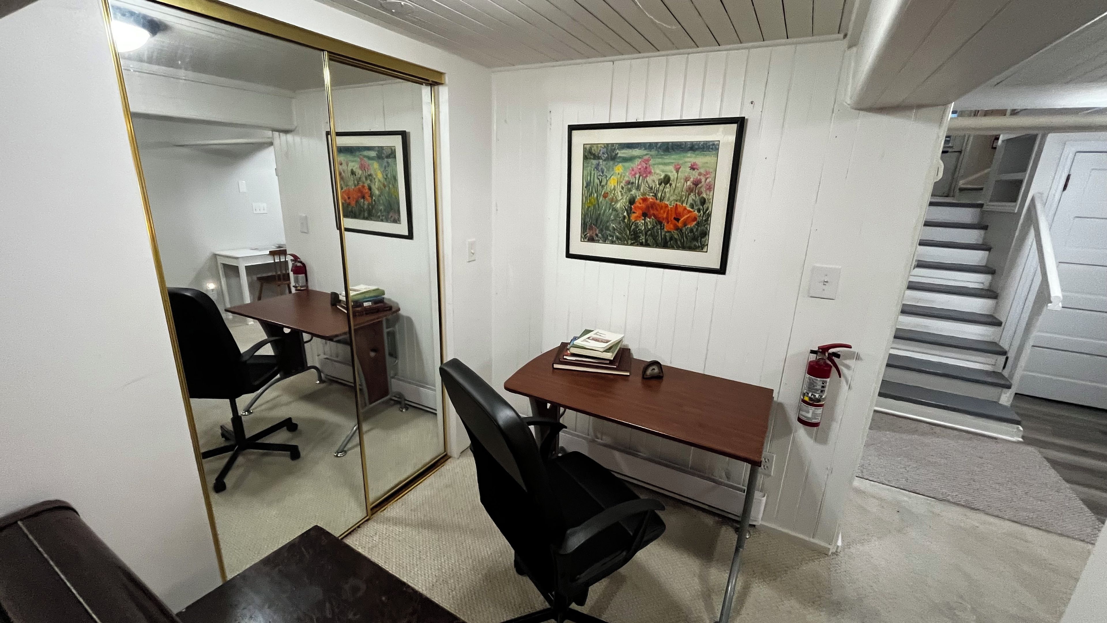 Una habitación con escritorio, silla, espejo y un cuadro en la pared.