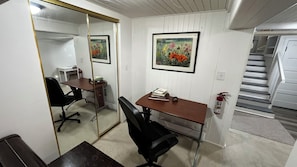 A room with a desk, chair, a mirror, and a framed painting on the wall.