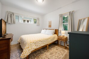 Une chambre à coucher comprenant un lit, une table de chevet, une commode, une fenêtre avec des rideaux et un miroir fixé au mur.