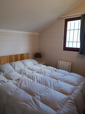 Een slaapkamer met een houten hoofdeinde, een raam met gordijnen en een radiator.
