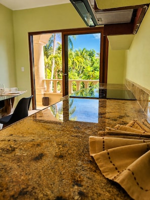 A kitchen with a large island, a dining table with chairs, and a view of a balcony with palm trees. - House with direct access to the beach (Puerto Aventuras)