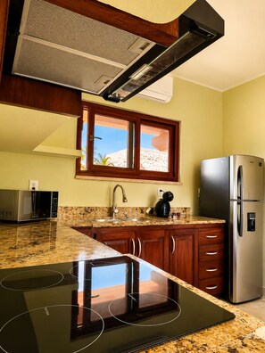 A kitchen with a built-in stove, a refrigerator, a microwave, and a window with a view of the outdoors. - House with direct access to the beach (Puerto Aventuras)