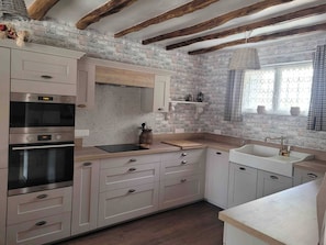 A kitchen with white cabinets, a built-in oven, and a window with curtains. - Aponem Guesthouse, a charming 4-star property (Savignac-les-Églises)