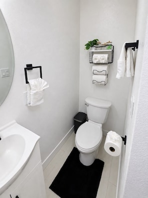 Ein modernes Badezimmer mit Toilette, Bidet und Waschbecken. Auf dem Boden liegt ein schwarzer Teppich und Handtücher hängen an einem Handtuchhalter.